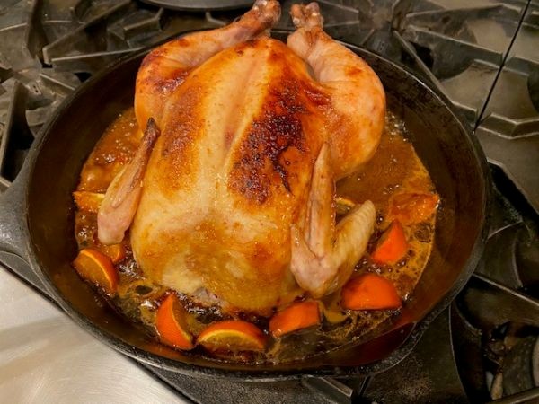 Color image of a roast chicken with carrots in a cast iron pan on a gas stove
